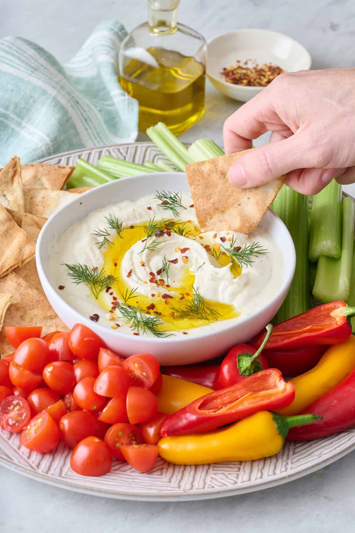 Hand dipping a pita chip into feta dip surrounded by veggies.