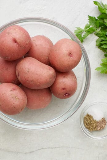 Ingredients for recipe: garlic cloves, grated parmesan, whole red potatoes, fresh parsley, seasonings, and oil.