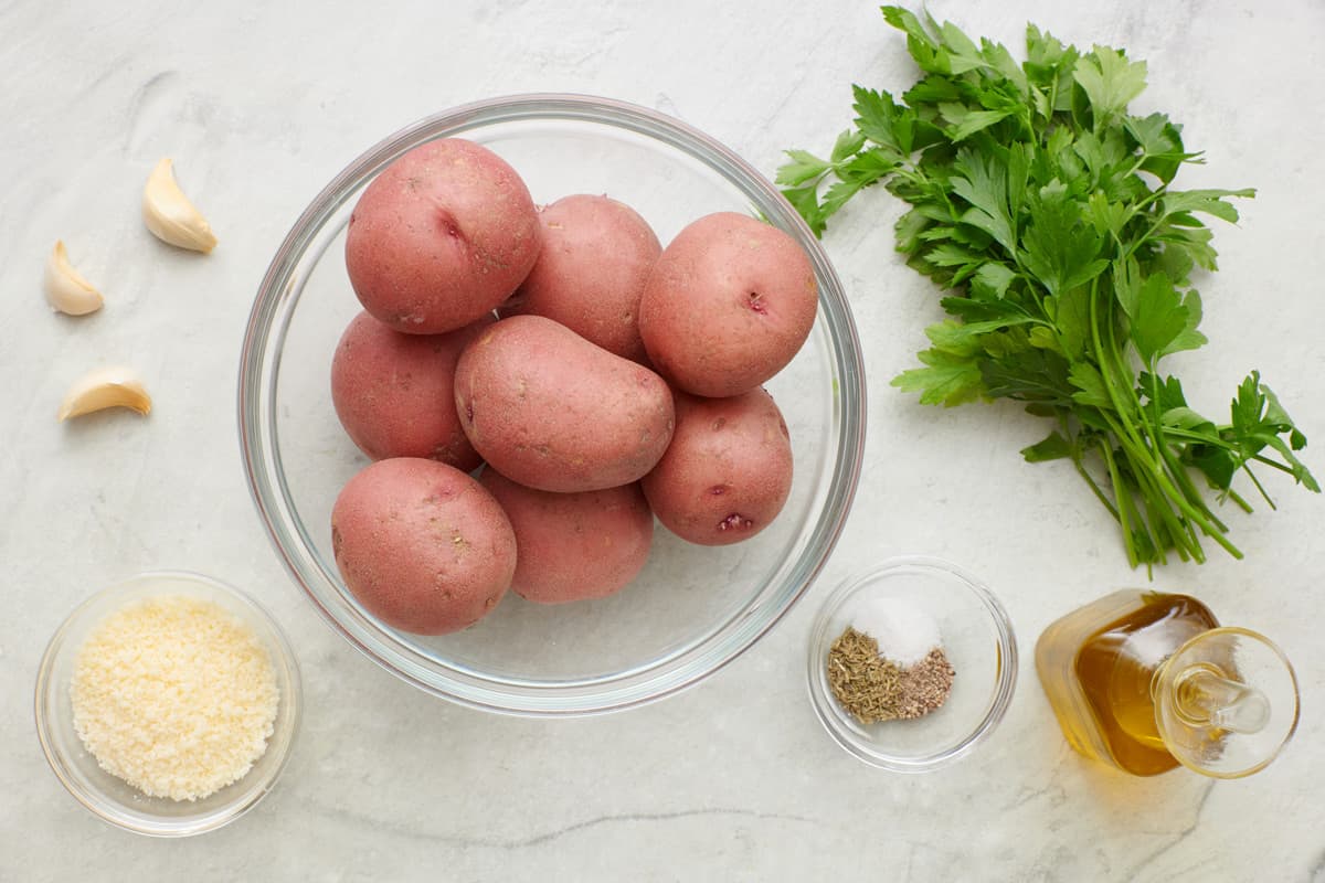 Ingredients for recipe: garlic cloves, grated parmesan, whole red potatoes, fresh parsley, seasonings, and oil.