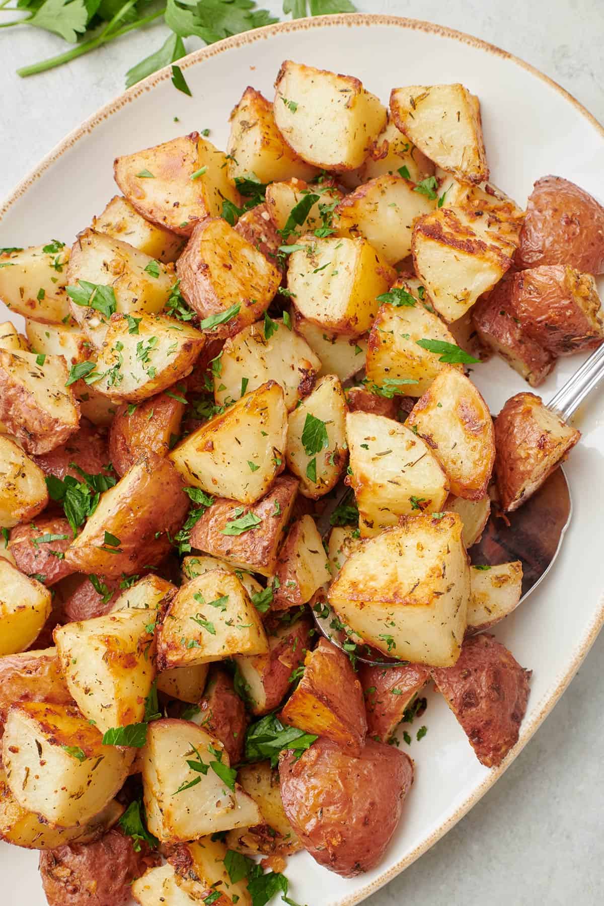 Close up shot of the garlic roasted potatoes garnished with fresh chopped parsley and a serving spoon dipped in.