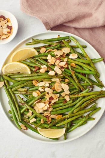 Green beans with almonds on a serving plate with lemon wedges.