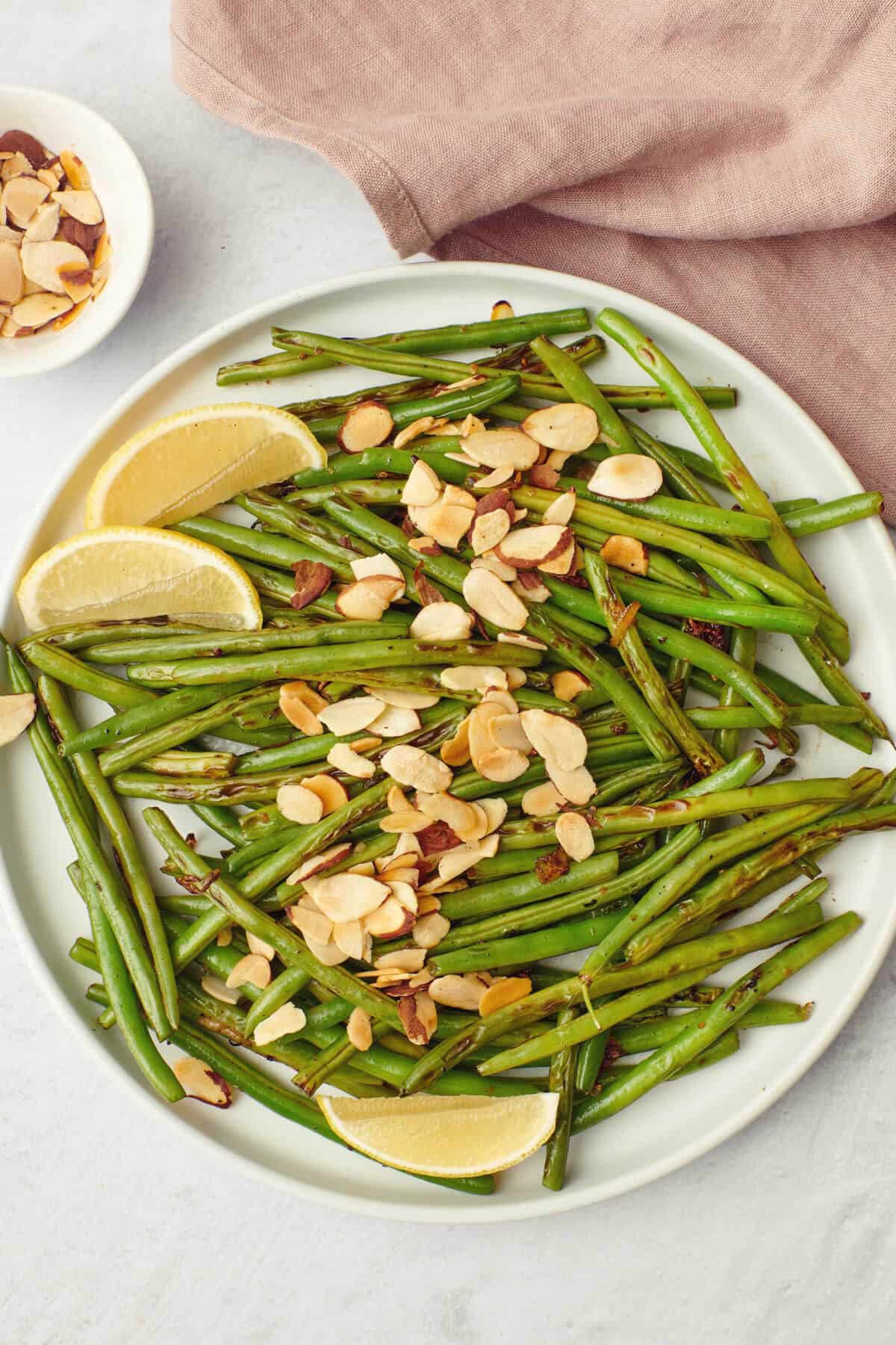 Close up of green beans with almonds with parmesan cheese and lemon wedges