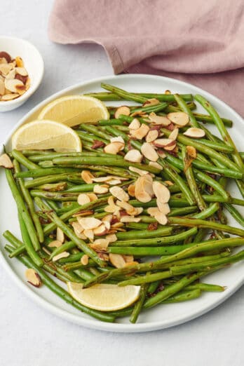 Green bean almondine on a plate with lemon wedges.