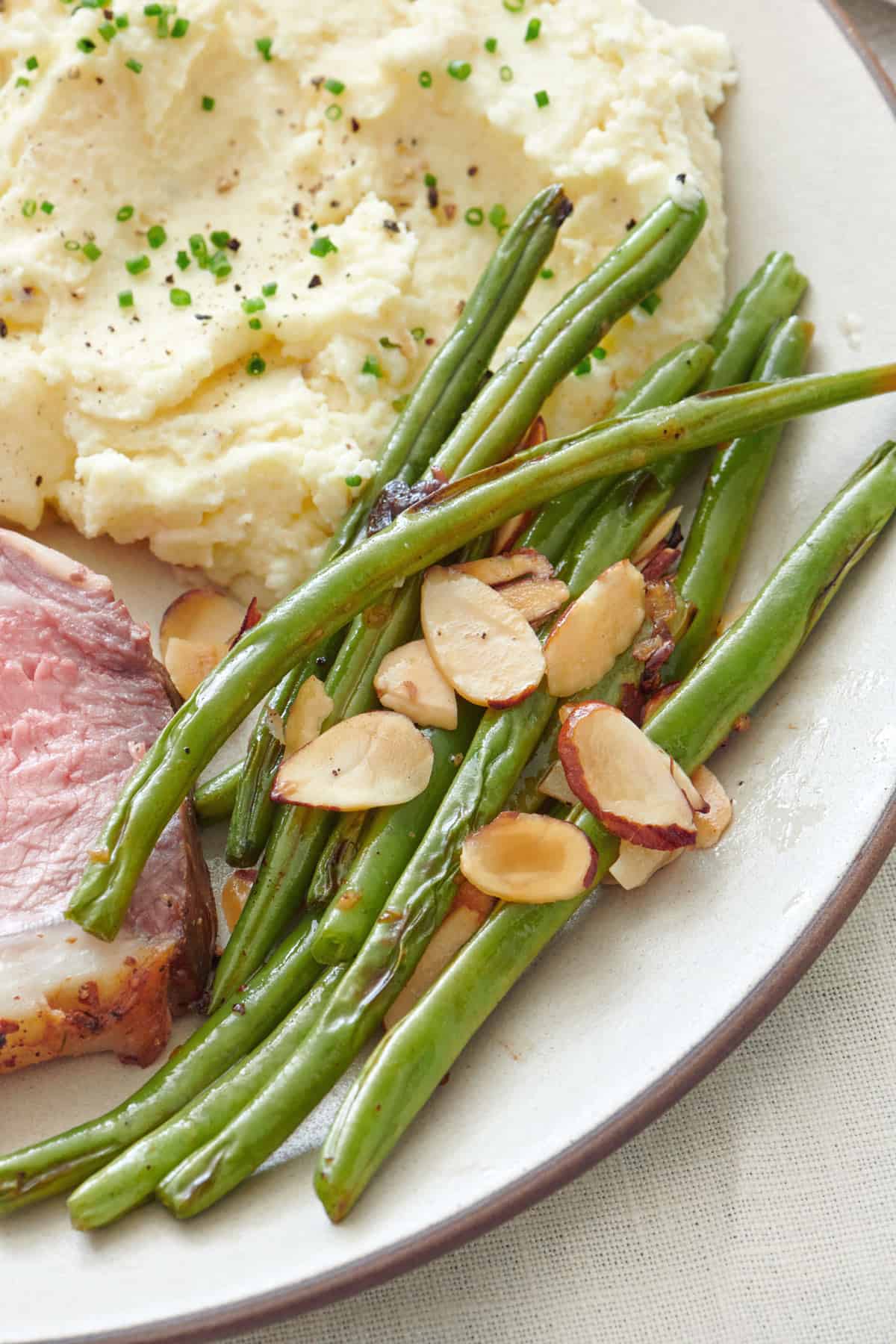 Serving of green beans on a Thanksgiving plate with mashed potatoes and prime rib.