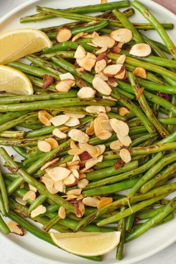 Close up of green beans with almonds with lemon wedges.