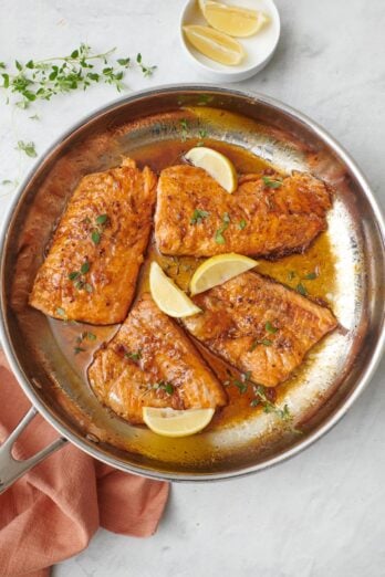 4 honey lemon salmon fillets in a skillet with sauce, garnished with fresh parsley and lemon wedges.