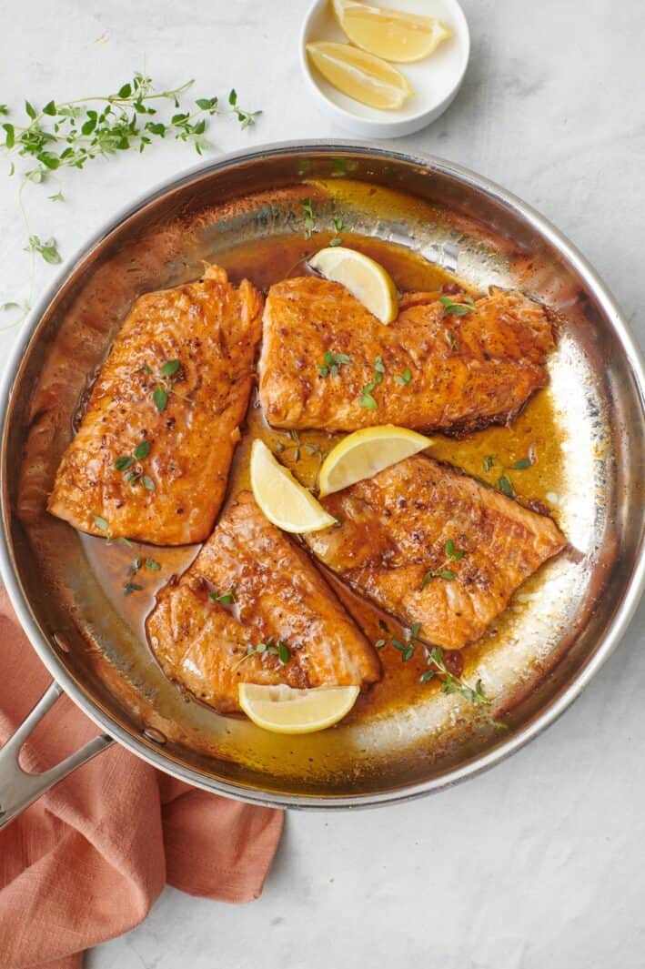 4 honey lemon salmon fillets in a skillet with sauce, garnished with fresh parsley and lemon wedges.