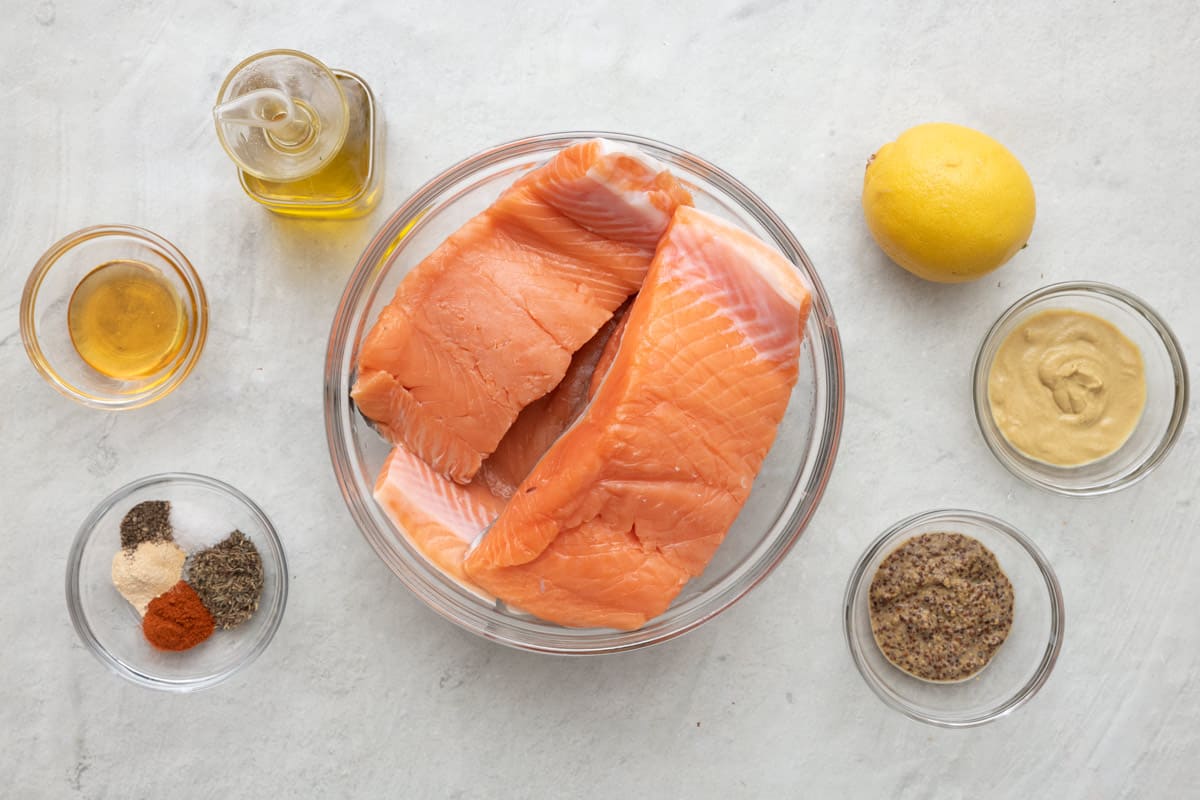 Ingredients for recipe: bowl of 4 salmon fillets, oil, honey, spices, lemon, dijon mustard, and whole grain dijon mustard.