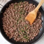 Ground beef in a skillet garnished with fresh parsley and a wooden spatula dipped in.