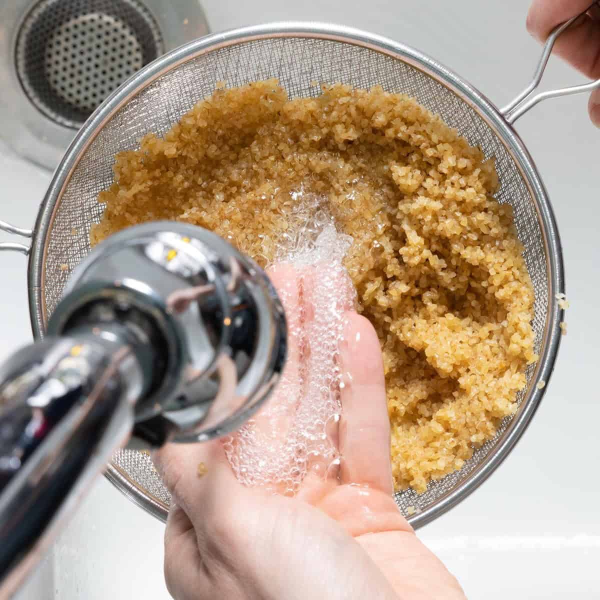Bulgur in a fine mesh sieve under running water with hand agitating it.