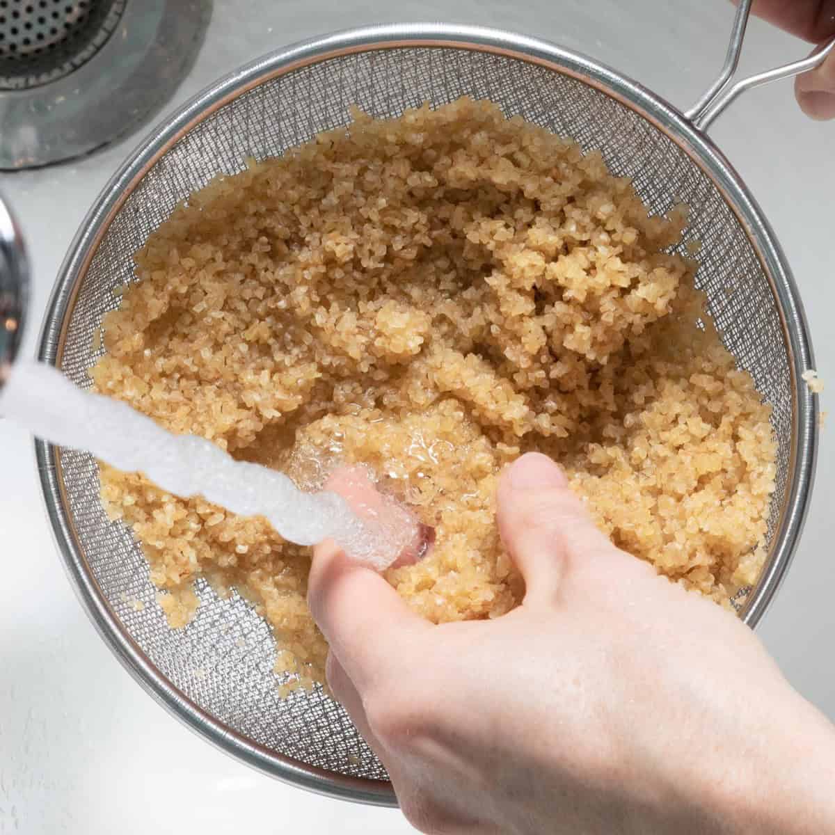 Bulgur in a fine mesh sieve under running water with hand agitating it.