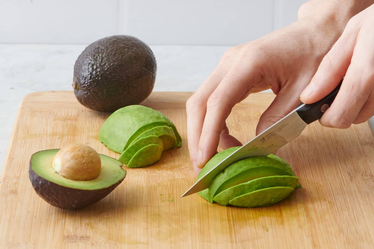 Slicing an avocado into slices with more avocados around.