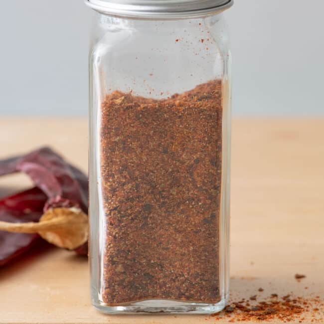 Homemade chili powder in a spice jar with dried chilis nearby.