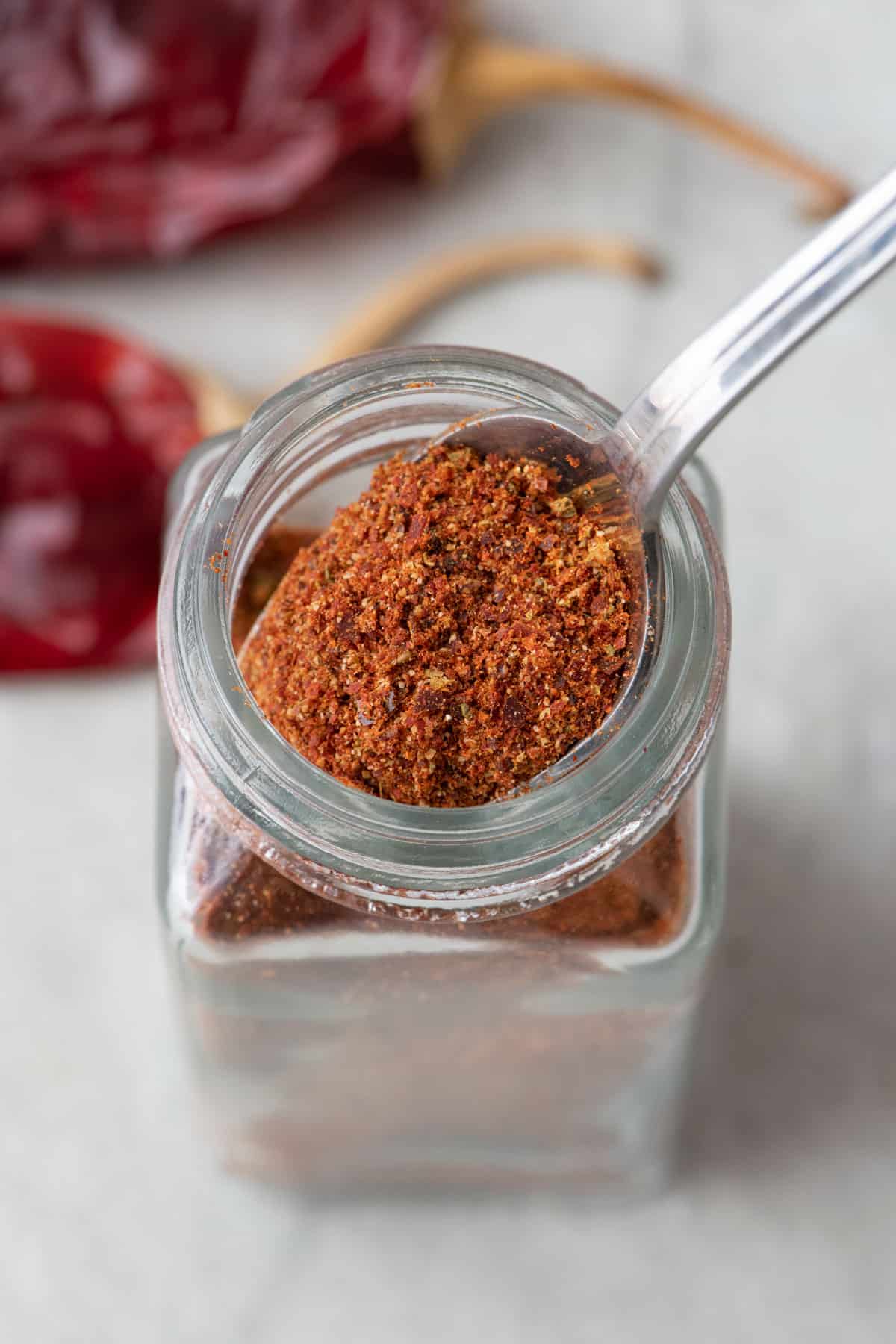Top down view of a spoon scooping out chili powder from spice jar.