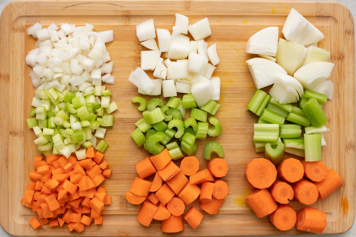 3 different cuts of a mirepoix vegetables lined up on a cutting board: small diced, medium-sized chunks, and large chunks.