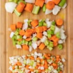 Three different sized blends of carrots, onions, and celery for a mirepoix lined up on a cutting board in rows.