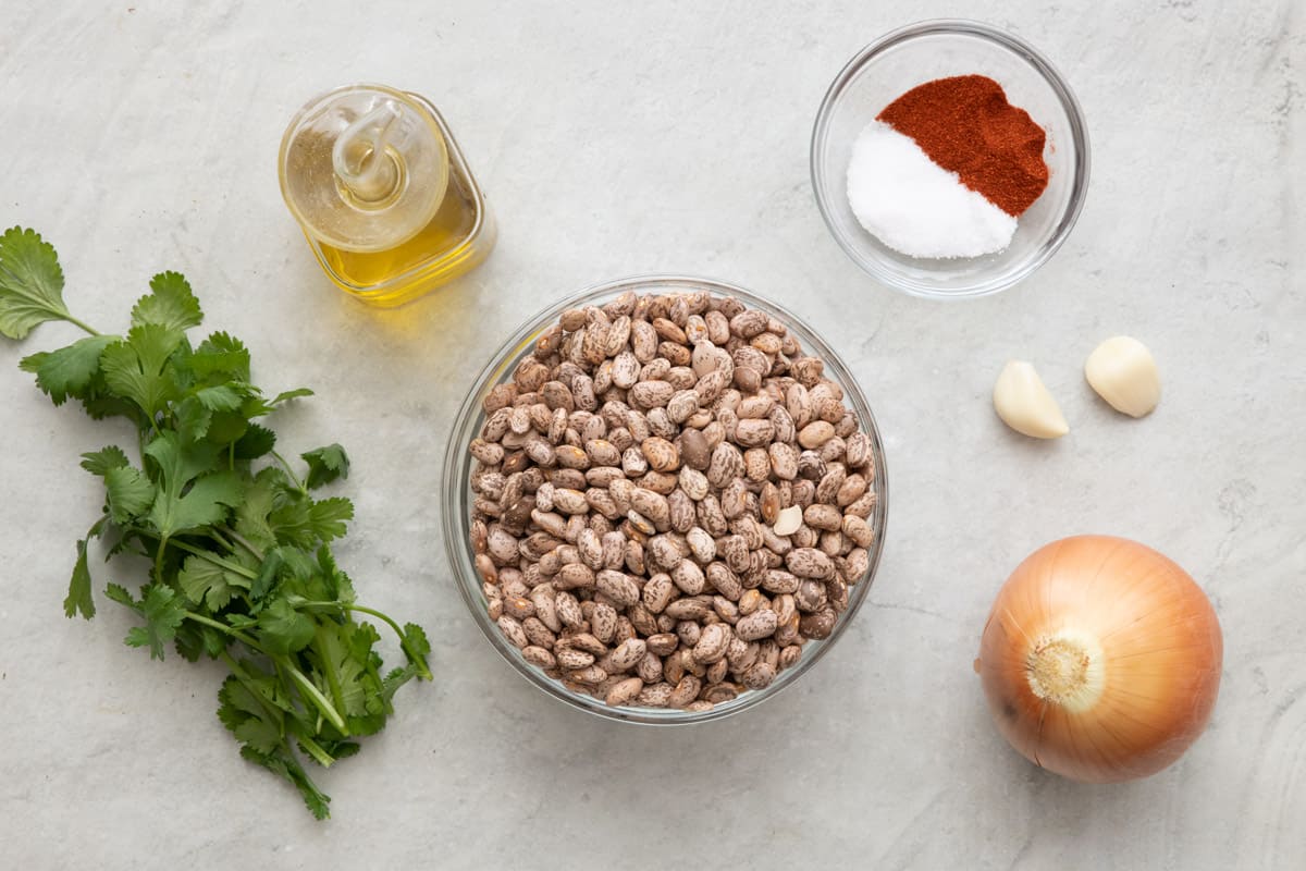 Ingredients for recipe: fresh cilantro, oil, dry pinto beans, paprika and salt, garlic cloves, and a yellow onion.