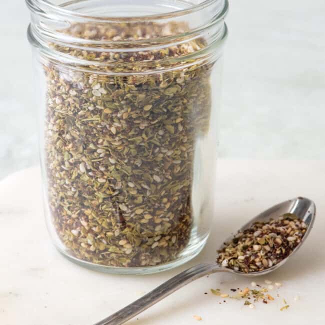Homemade Za'atar seasoning in a spice jar with a spoonful of spice next to it.