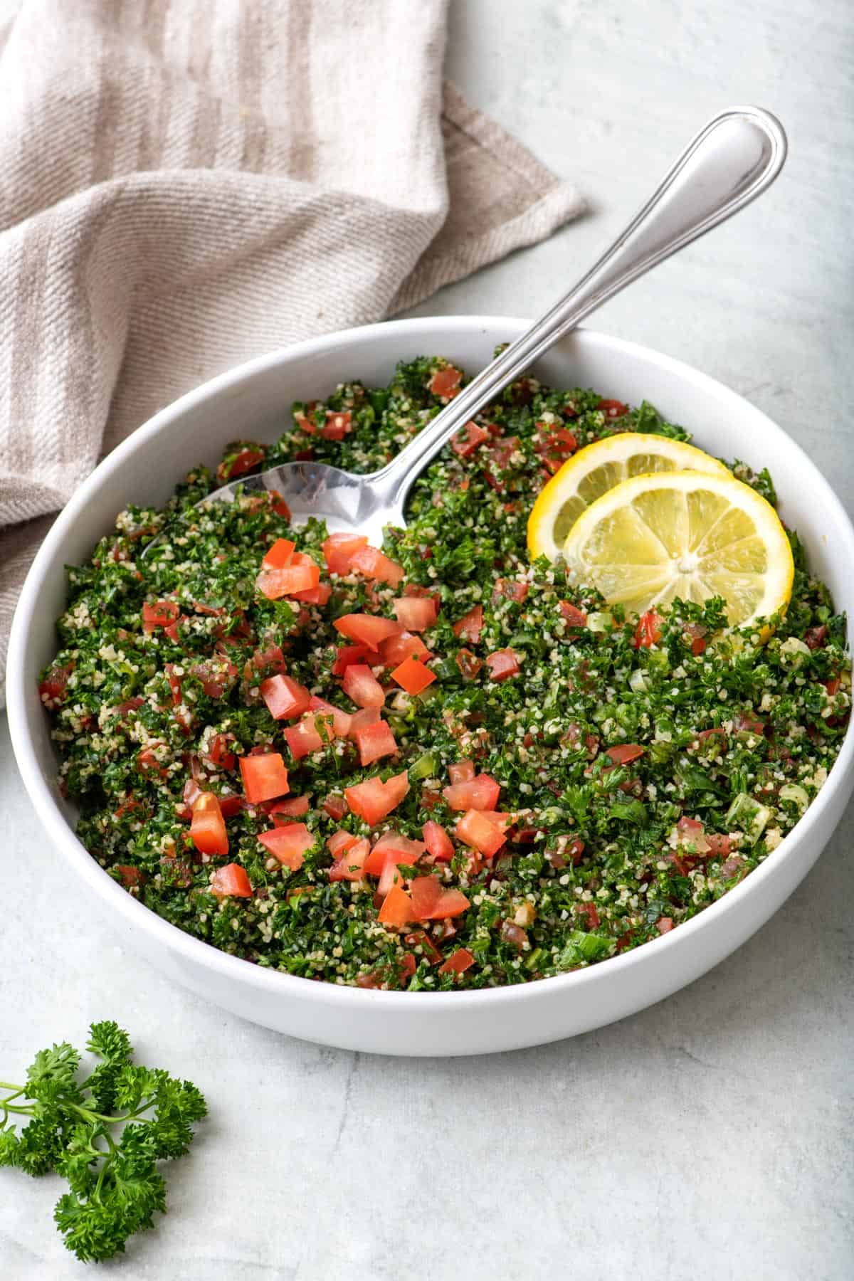 Tabbouleh salad in a large salad bowl with a spoon dipped in with a few lemon slices.