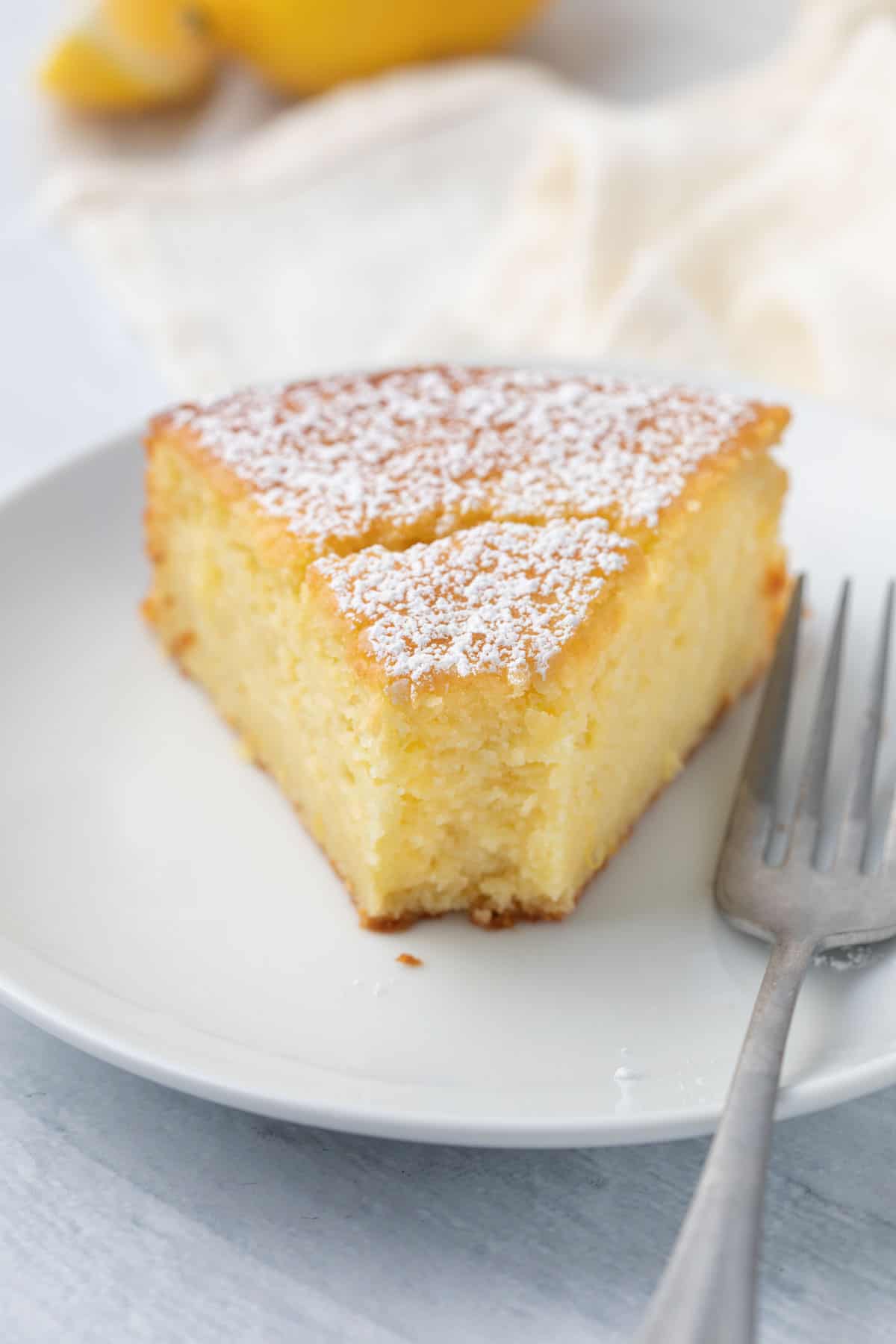 Straight on view of a slice of lemon ricotta cake with a bite taken out and fork resting on plate.
