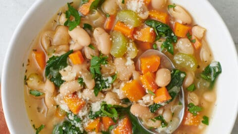 Mediterranean white bean soup in a bowl with a spoon lifting up a bite.