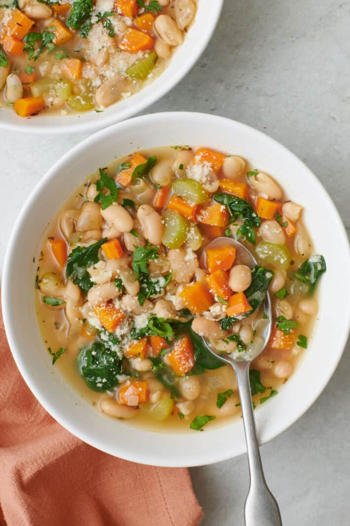 Mediterranean white bean soup in a bowl with a spoon lifting up a bite.