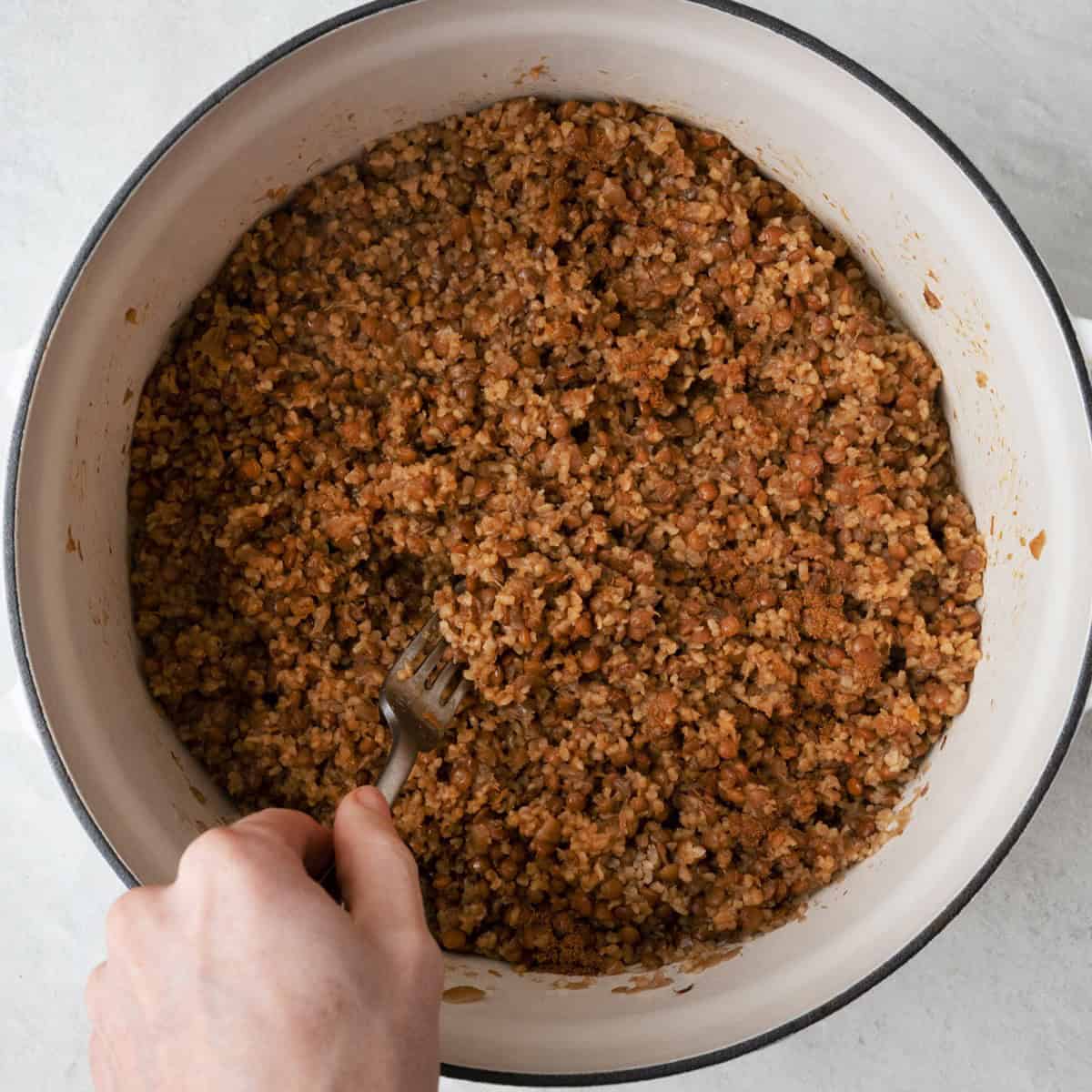 Fluffing lentils and rice with a fork after cooked with cumin sprinkled on top.