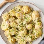 Mustard potato salad in a large shallow serving bowl with a wooden spoon nearby.