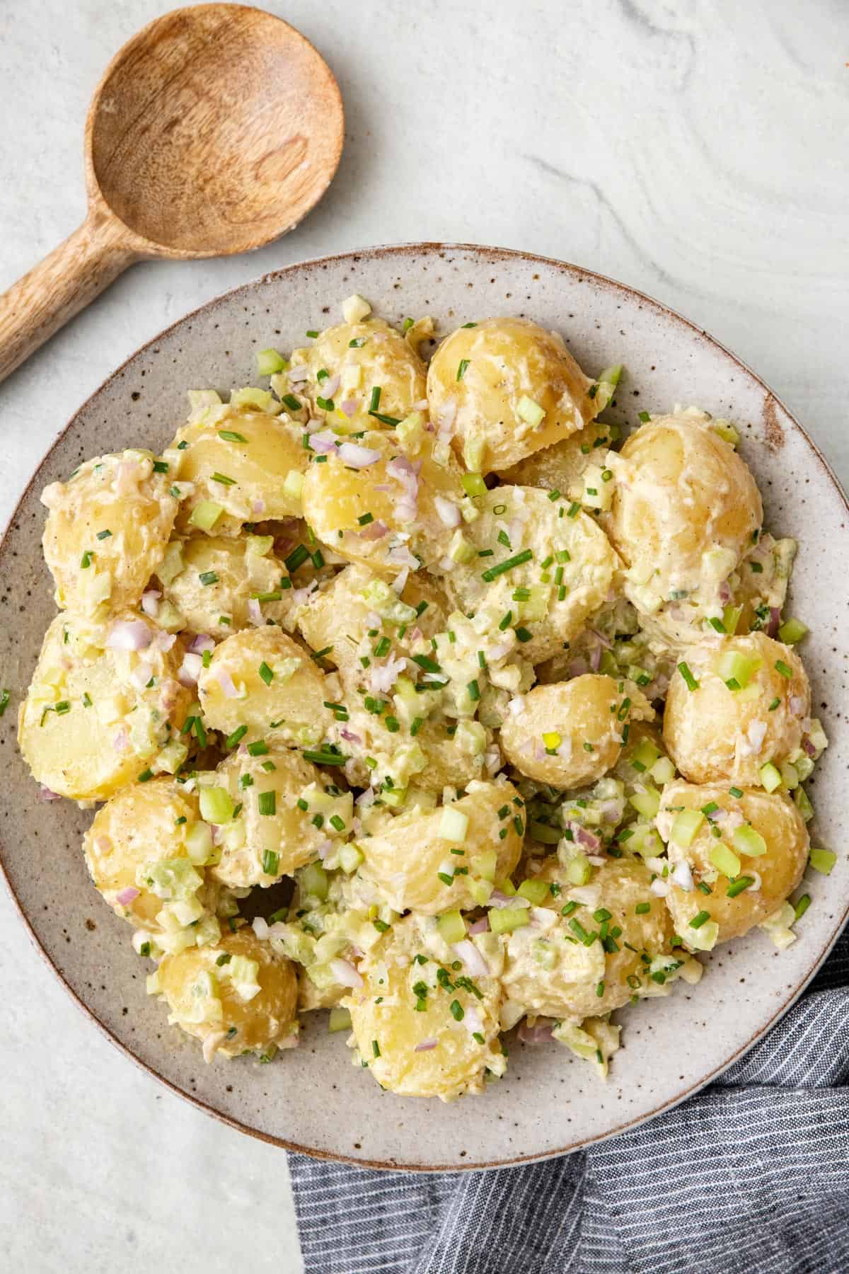 Mustard potato salad in a large shallow serving bowl with a wooden spoon nearby.