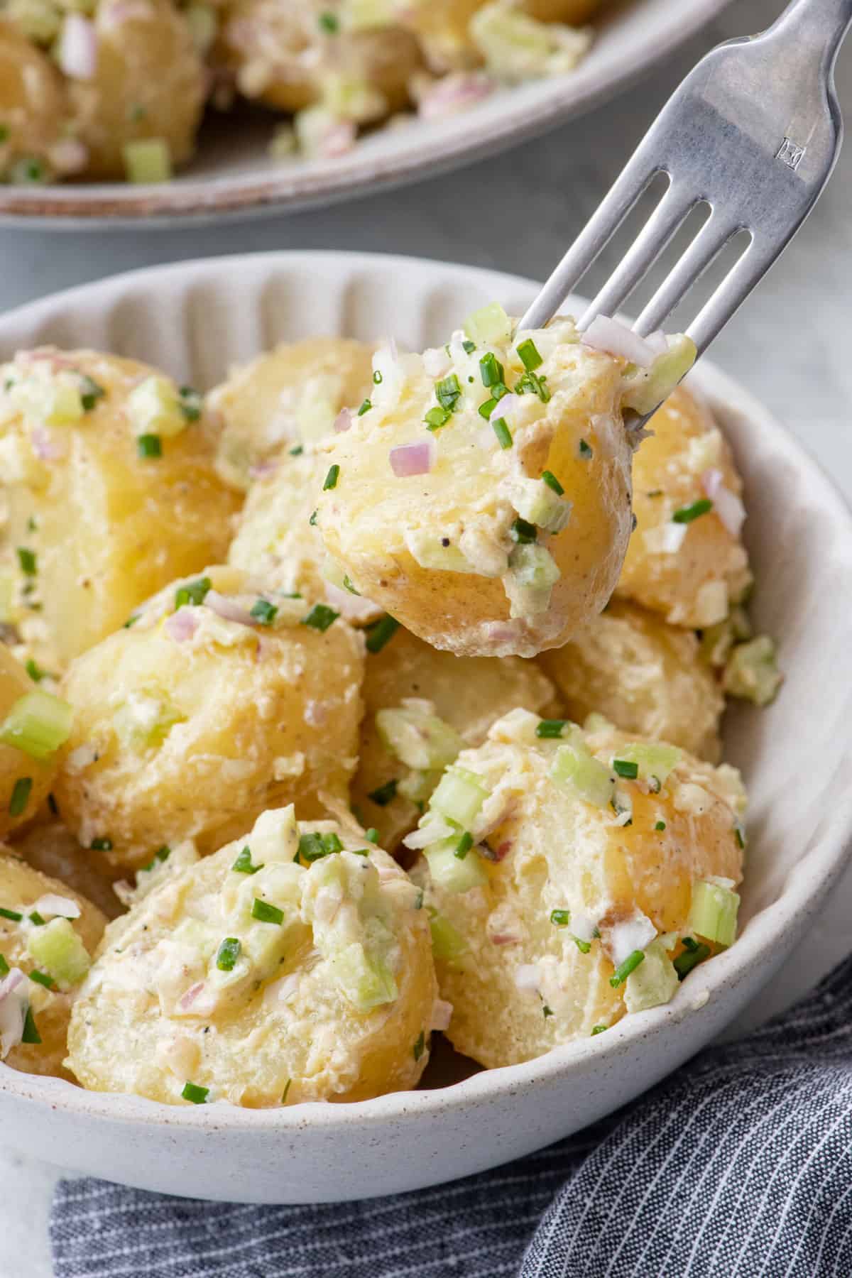 Potato salad in a bowl with a fork picking up a piece to show the light dressing and finely diced onions, celery, and chives.