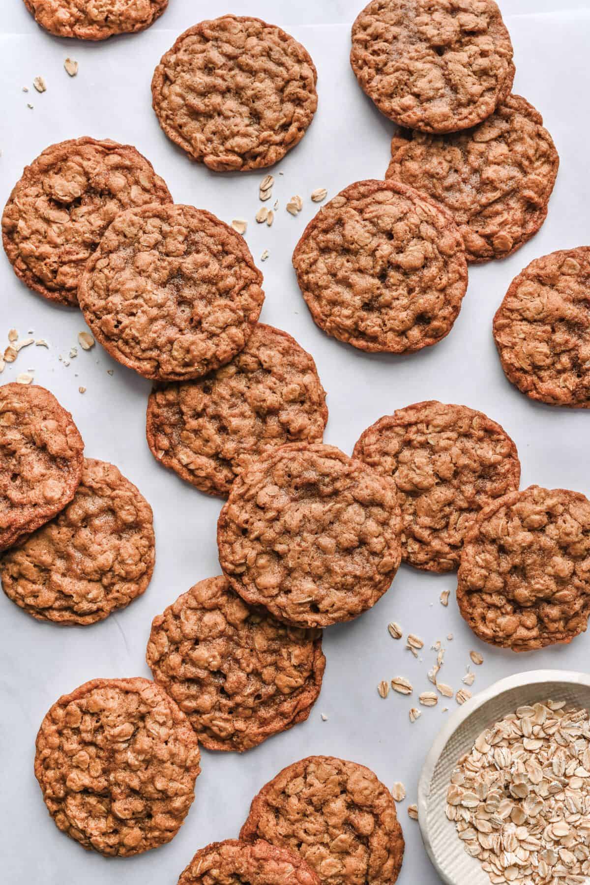Oatmeal cookies on parchment paper with a small bowl of oats.