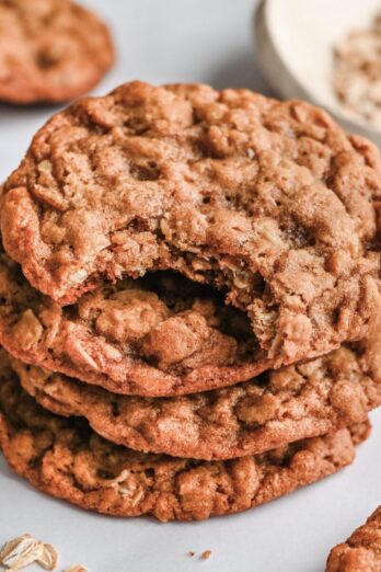 Oatmeal cookies stacked up with one having a bite taken out.