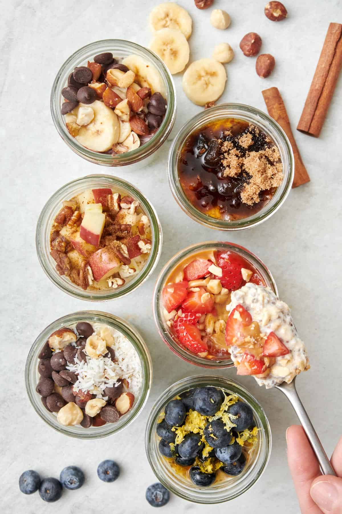 Overhead shot of 6 different overnight oat recipes with a spoon lifting up a bite from one.
