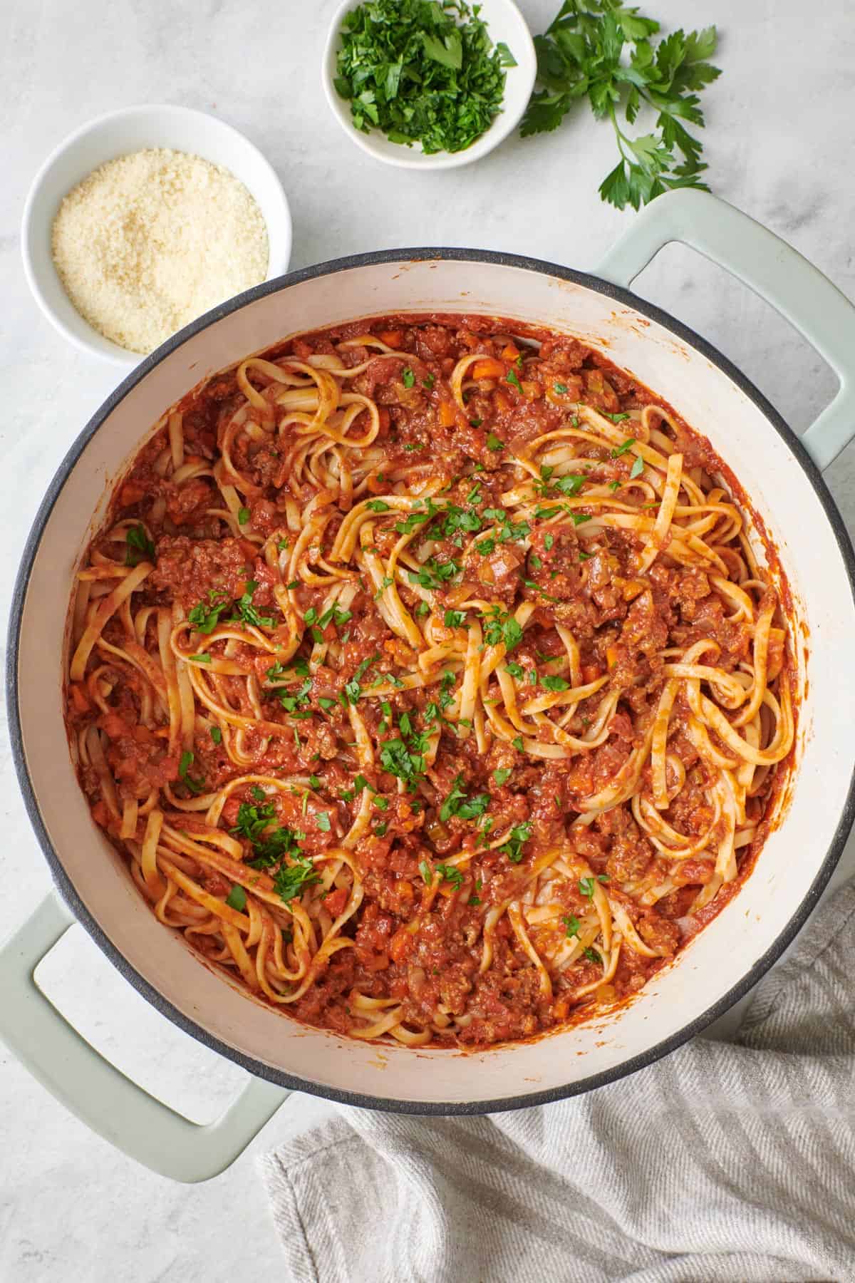 Pasta Bolognese in a large pan topped with fresh basil leaves with a wooden spoon