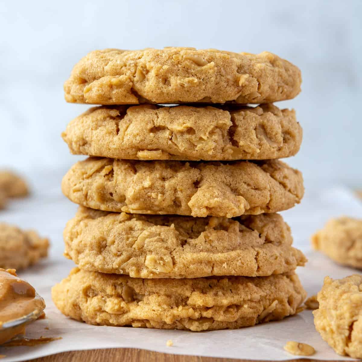 Peanut butter oatmeal cookies on parchment paper with a small jar of peanut butter and a spoon nearby.