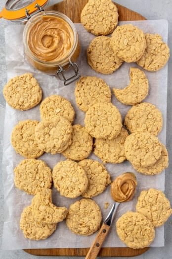 Peanut butter oatmeal cookies with a small jar of peanut butter and a spoon on parchment paper.