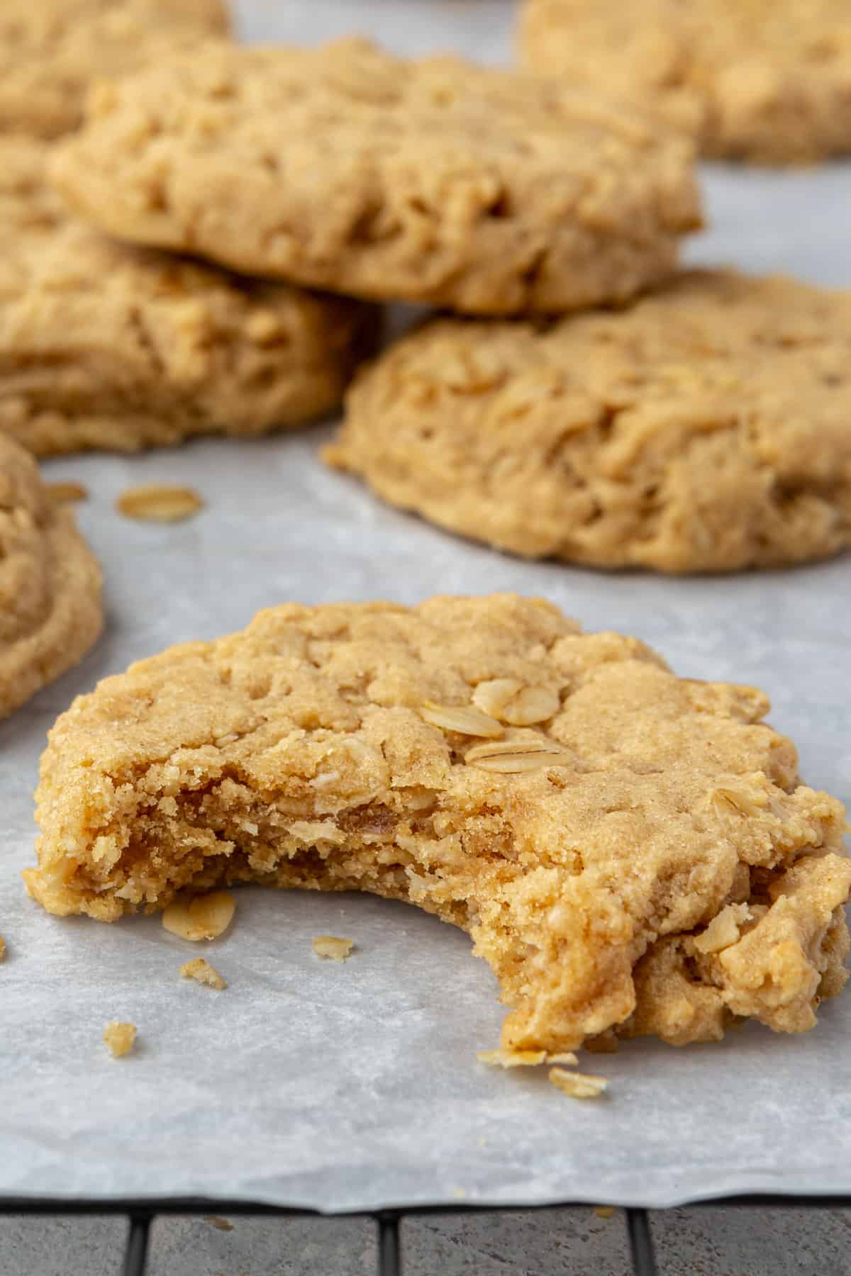 A peanut butter oatmeal cookie with a bite taken out with other cookies on parchment paper.