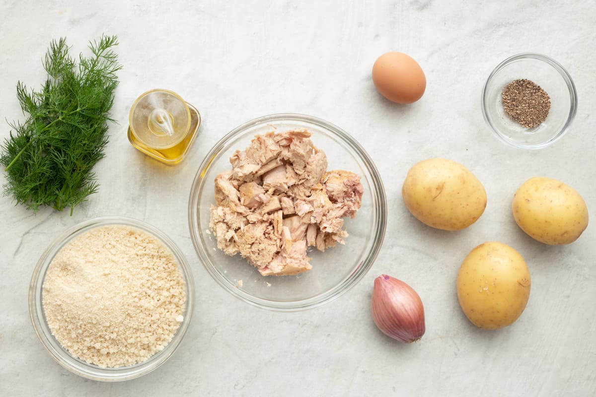 Ingredients for recipe before prepping: fresh dill, breadcrumbs, tuna, oil, shallot, potatoes, an egg, and seasoning.