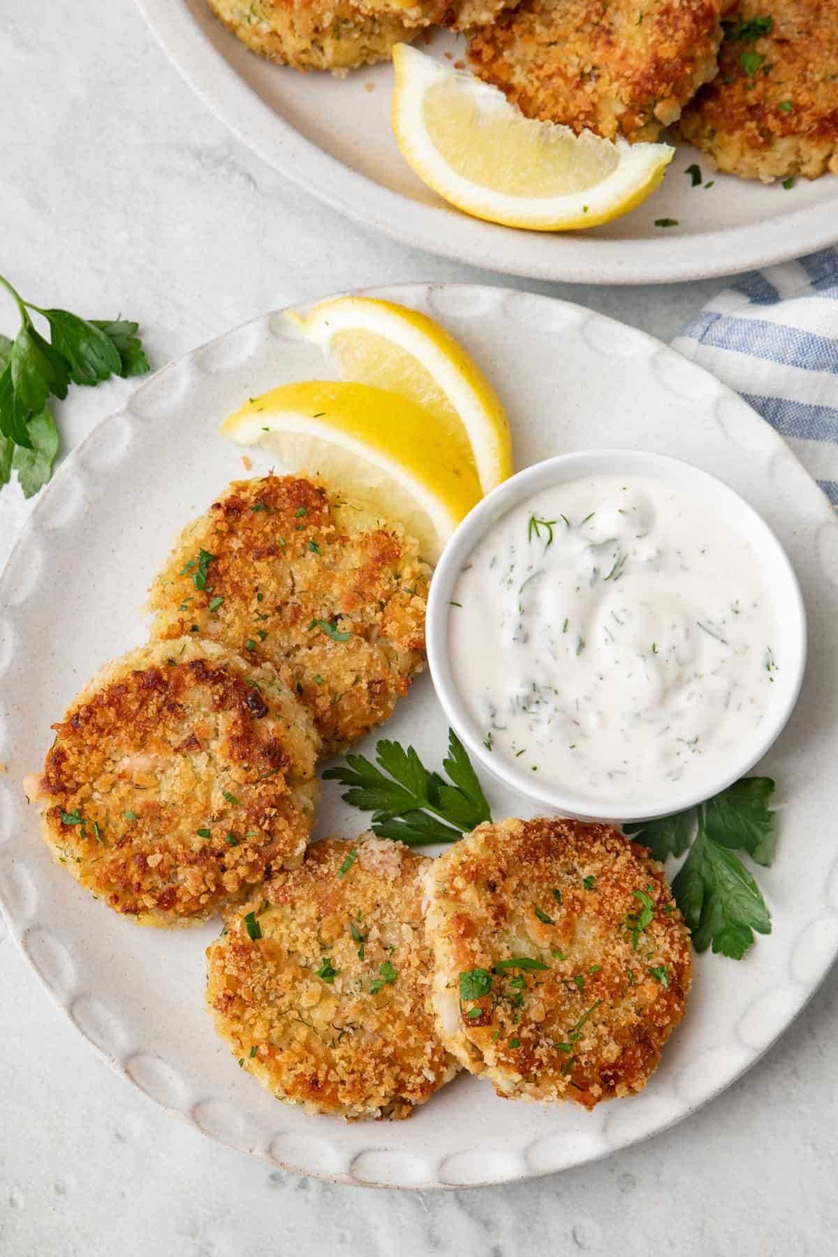A few tuna potato cakes on a small plate with tzatziki sauce and lemon wedges.