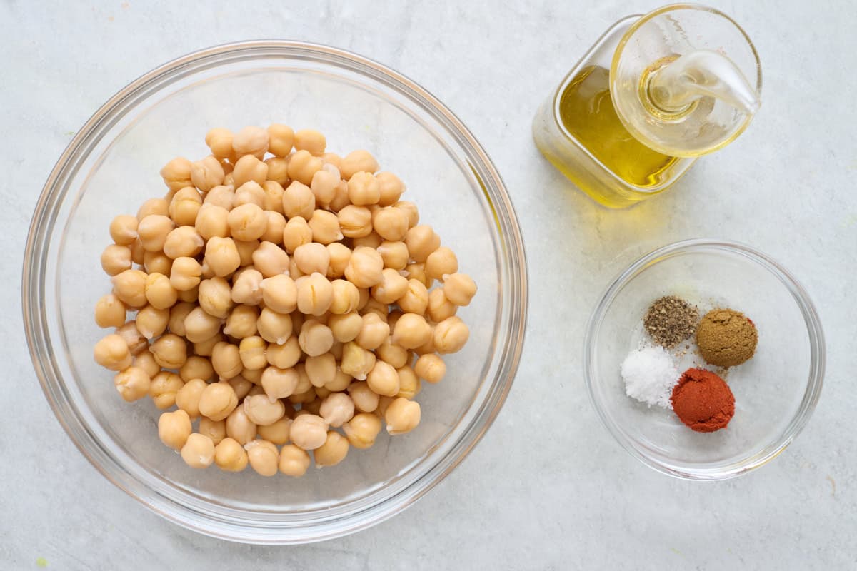 Ingredients for recipe in separate containers: bowl of chickpeas, spices, and oil.