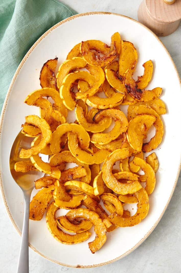 Roasted delicata squash slices on a large oval platter with a serving spoon.