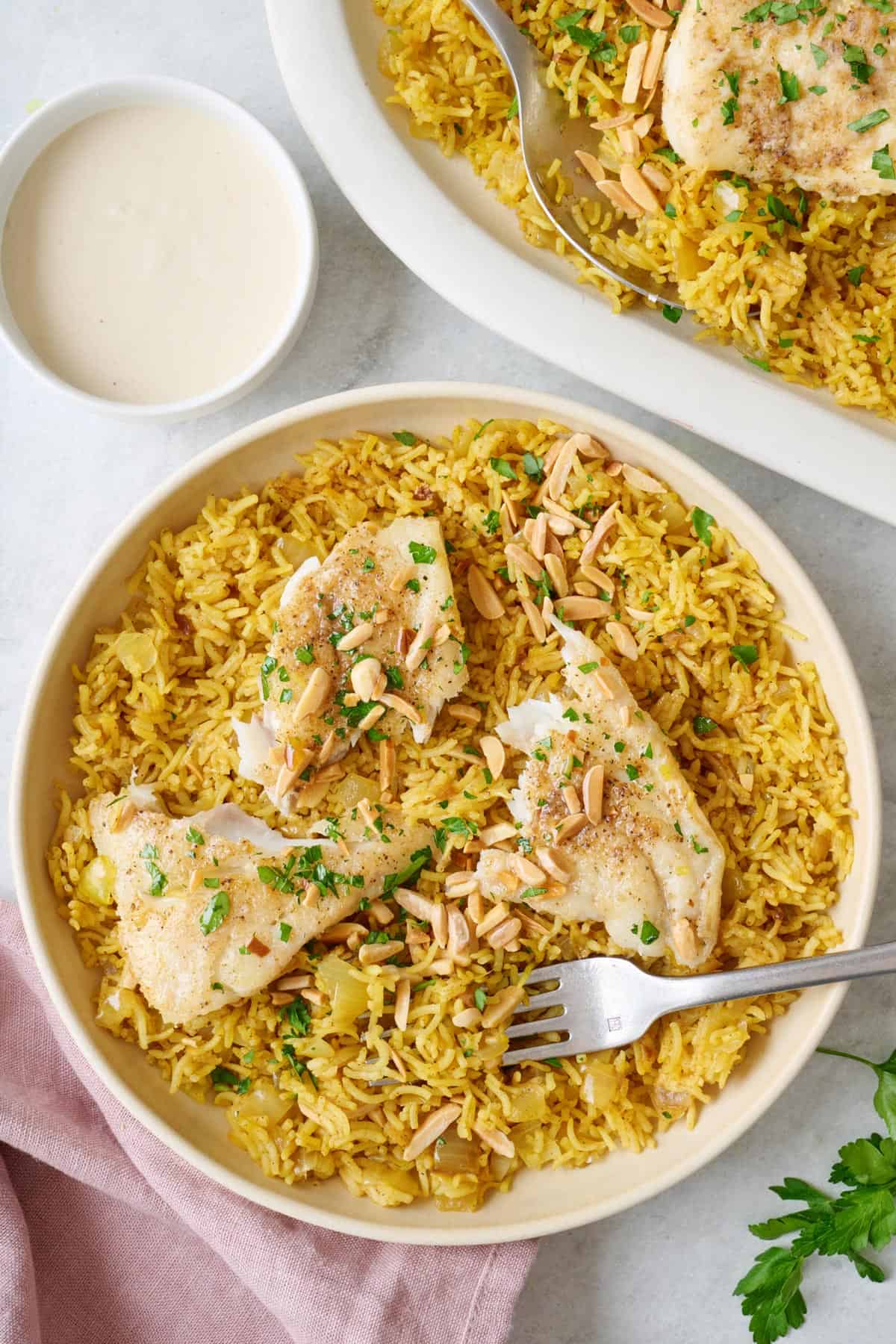 Lebanese rice and fish, or Sayadieh, on a plate with a side of tahini dressing.