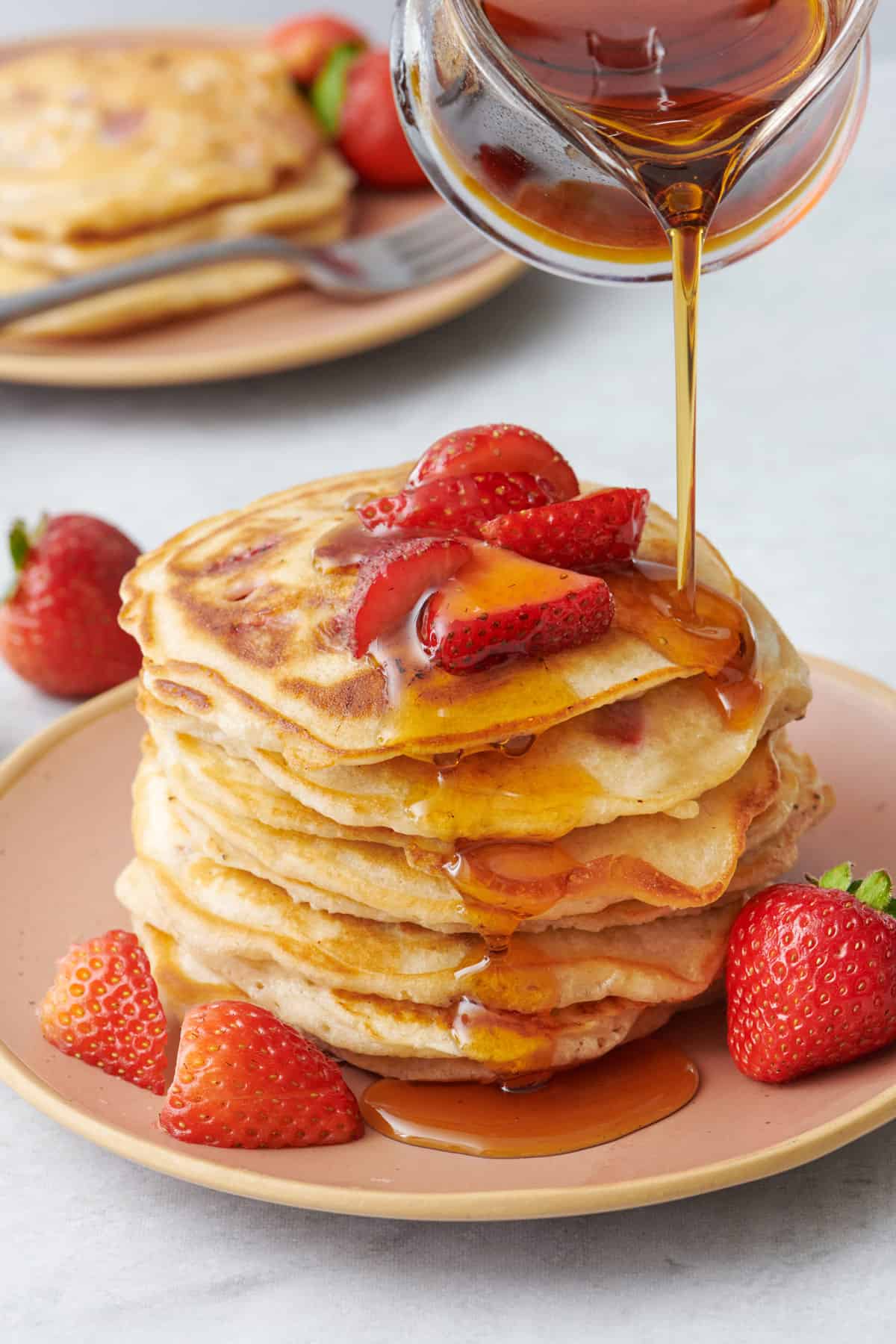 Pouring maple syrup on top of a stack of fresh strawberry pancakes.