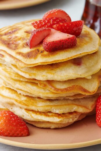Stack of fresh strawberry pancakes on a plate with more fresh strawberries around.
