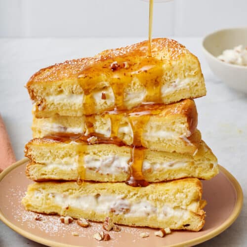 Final plating of the stuffed french toast with two stacked on top of each other, topped with bananas and maple syrup getting drizzled on top