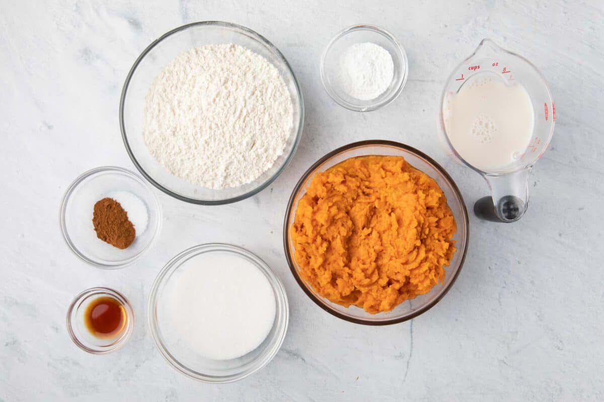 Ingredients for recipe in individual bowls: flour, salt and cinnamon, vanilla extract, sugar, baking powder, roasted mashed sweet potatoes, and milk.