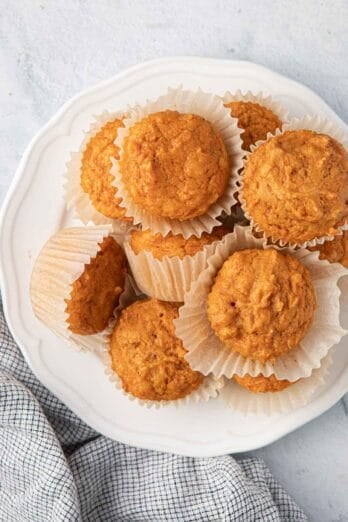 Soft and moist sweet potato muffins stacked on a plate with the paper liner pulled away from a few.