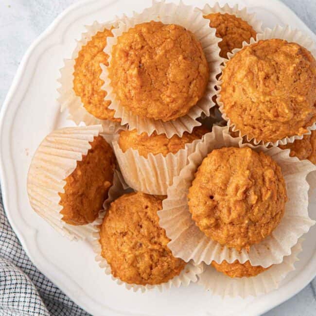 Soft and moist sweet potato muffins stacked on a plate with the paper liner pulled away from a few.