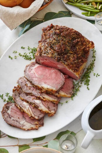 Prime rib on a serving platter cut halfway into thick slices to show a pink medium rare temperature.