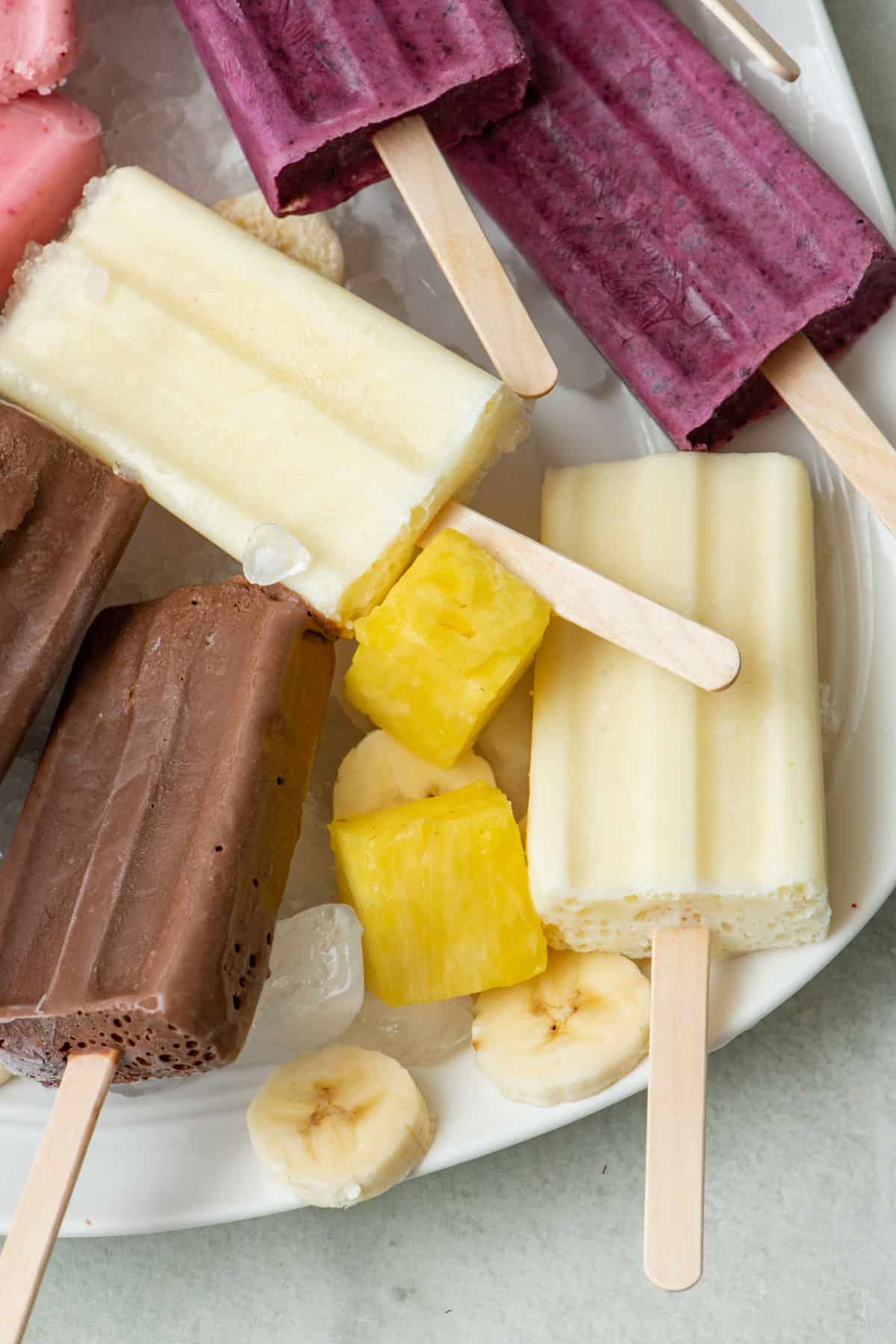 Frozen pineapple yogurt popsicles on a tray of ice with extra pineapple chunks around.